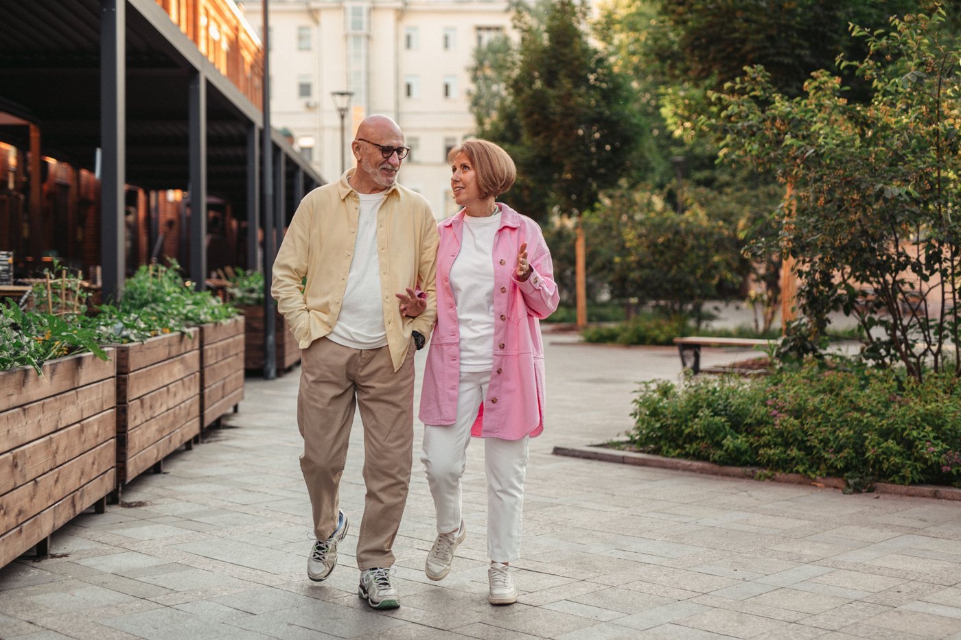 Un couple de seniors se promène dans un quartier arboré.